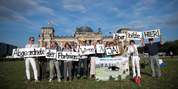 Menschen stehen mit Plakaten vor dem deutschen Bundestag. Sie demonstrieren für das Denkmal für die deutsche Einheit