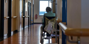 Eine Patientin im Rollstuhl steht alleine auf einem Krankenhausflur.