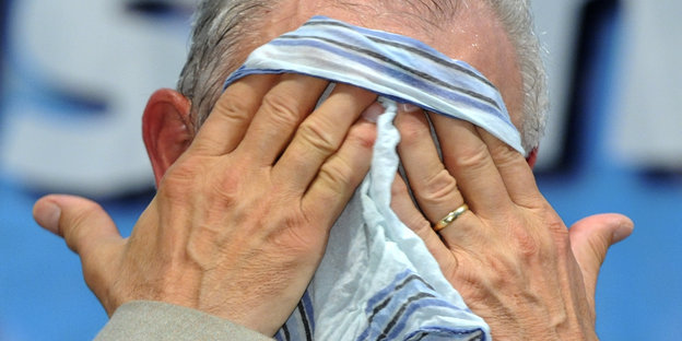 Ein Mann wischt sich mit einem Stofftaschentuch das Gesicht ab