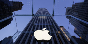 Ein angebissener Apfel, das Sysmbol des US-Konzerns Apple, hängt an einem Fenster. Im Hintergrund ist ein Wolkenkrazer zu sehen.