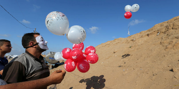 Zwei junge Palästinenser, von denen einer eine weiße Maske vor dem Gesicht trägt, halten mit Helium gefüllte Ballons, die sie mit Brandsätzen bestückt über die Grenze nach Israel schicken