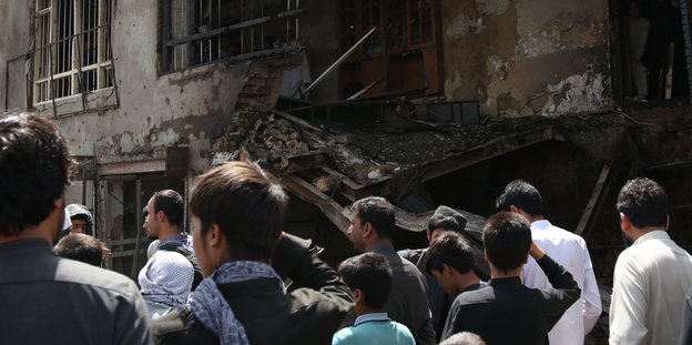 Menschen stehen vor einem rußgeschwärzten Gebäude, auf das offenbar ein Anschlag stattgefunden hat