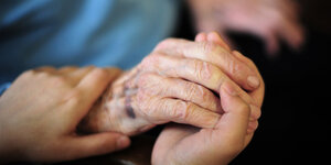 Die Hände einer jüngeren Person halten die Hand einer alten Person