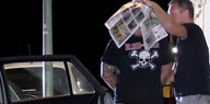 Ein Mann mit tätowierten Armen und Beinen, sein Gesicht unter einer Zeitung verdeckt