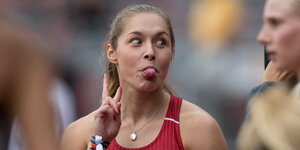 Gina Lückenkemper macht ein Victory-Zeichen und streckt einer anderen Sportlerin die Zunge heraus