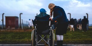 Eine Frau in einem Rollstuhl ist von hinten zu sehen, neben ihr steht eine zweite Frau