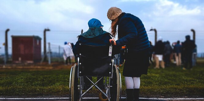 Eine Frau in einem Rollstuhl ist von hinten zu sehen, neben ihr steht eine zweite Frau