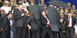 Menschen in Uniformen, in der Mitte wird Nicolas Maduro von Soldaten mit kugelsicheren Planen geschützt