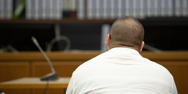 Ein kräftiger Mann mit weißem Hemd sitzt in einem Gerichtssaal.