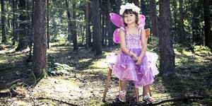 Ein Kind im rosa Feenkostüm sitzt auf einem Hocker im Wald