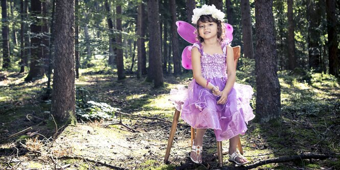 Ein Kind im rosa Feenkostüm sitzt auf einem Hocker im Wald