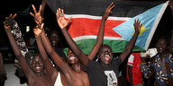 Mehrere Männer heben vor einer südsudanesischen Flagge die Arme