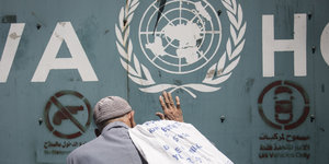 Ein älterer Mann mit blauem Arbeiterhemd und Mütze und mit einem Plastiksack über der Schulter klopft mit flacher Hand an die Tür des UN-Quartiers für palästinensische Flüchtlinge
