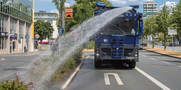 Ein Wasserwerfer der Polizei bespritzt den Grünstreifen einer Straße mit Wasser