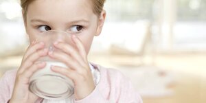 ein Kind hält ein Glas voll Milch an seinen Mund und trinkt