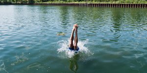 Die Beine eines Mannes ragen aus dem Wasser, in das er gerade mit einem Kopfsprung eingetaucht ist
