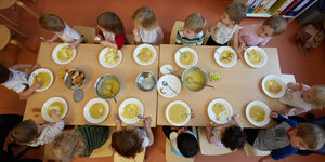 Kinder sitzen in einer Kita an einem Tisch und essen Suppe.