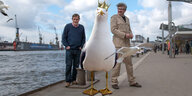 Andreas Dorau und Gereon Klug stehen mit einer Riesenmöwe mit Krone am Hamburger Hafen (Fotomontage)