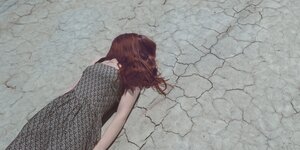 Eine Frau liegt auf trockenem Boden und hat die Haare über dem Gesicht
