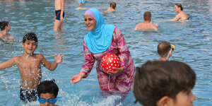 Eine Frau im Burkini spielt im Wasser mit Kindern.