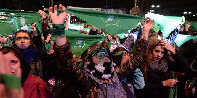 Frauen halten grüne Halstücher in die Luft