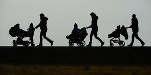 Drei Kinderwagen werden von vier Personen geschoben