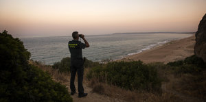 Ein Mann steht an einer Küste und guckt durch ein Fernglas auf das Meer