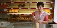 Eine Bäckereiverkäuferin steht hinter der Verkaufstheke und hält eine Tüte in der Hand