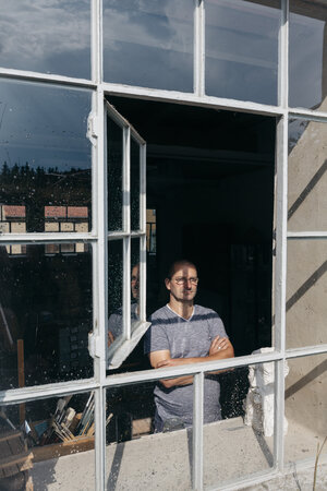 Ein Mann steht mit verschränkten Armen hinter einem geöffneten Fenster Ein Mann steht mit verschränkten Armen hinter einem geöffneten Fenster