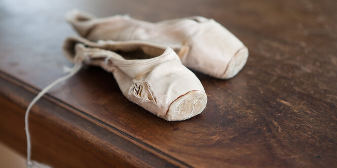 weiße Ballettschuhe liegen auf einem dunklen Holztisch