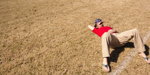 Ein Mannn liegt mit übers Gesicht gezogenem Käppi auf einem Feld
