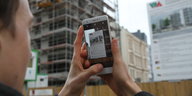 Ein Mann guckt auf ein Smartphone-Bildschirm. Er fotografiert eine Werbetafel