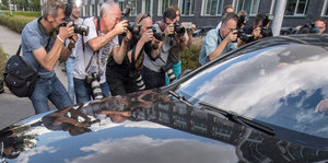 Eine Medienmeute beugt sich gierig über ein schwarzes Auto