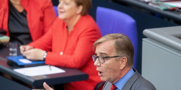 Dietmar Bartsch spricht im Bundestag, im Hintergrund sitzt Angela Merkel