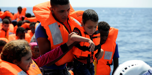 Ein Mann hebt einen kleinen Jungen in Rettungsweste auf ein Schiff