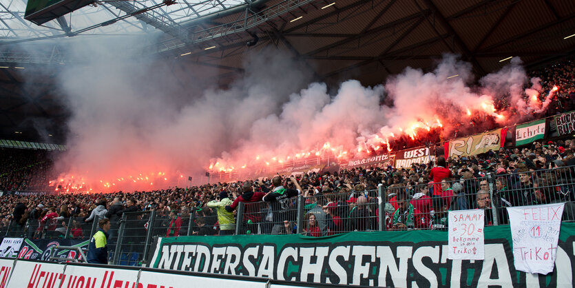 Im Fanblock eines Fußballstadions brennen mehrere Bengalos.