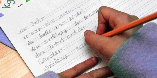 Ein Kind schreibt einen Text in ein Schulheft.