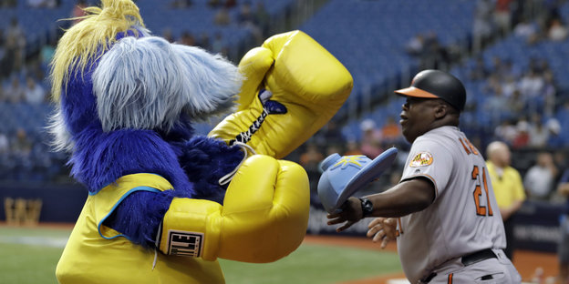 Ein gelb-blaues Maskottchen namens Raymond liefert sich einen spielerischen Boxkampf mit Wayne Kirby von den Baltimore Orioles