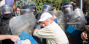 ein Mann mit weißer Baseballcap vor den Schutzschildern mehrerer Polizisten