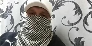 Der inhaftierte YouTuber vor einer Wand. Er trägt eine Kappe und ein Tuch, um sein Gesicht zu verschleiern.