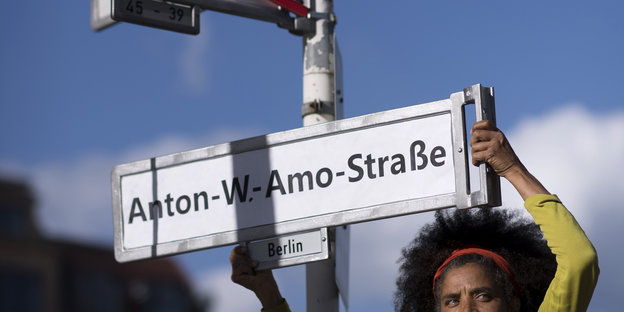 Eine Frau hält ein Straßenschild mit den Namen Anton-W.-Amo-Straße hoch