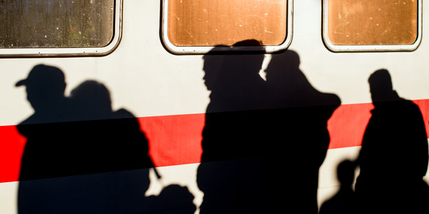 Vor einem Zug spiegeln sich die Schatten von Menschen