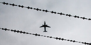 Ein Flugzeug fliegt über Stacheldraht am Himmel