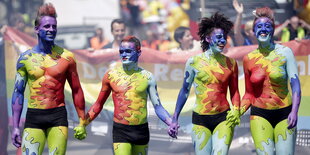 Vier Menschen halten sich an den Händen. Ihre Körper sind bunt angemalt.