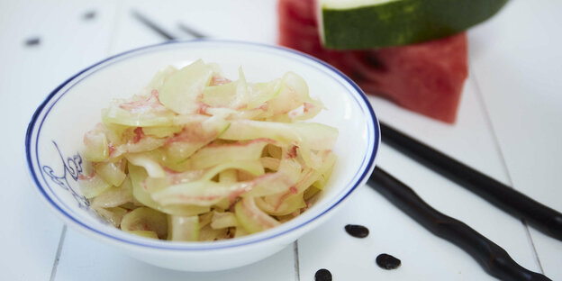 Ein Salat auf einem weißen Teller, daneben Stäbchen und Wassermelone