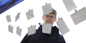 David Missal steht hinter einer Wäscheleine, auf der Postkarten aufgehängt sind