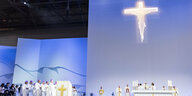 Katholische Würdenträger vor einer blau erleuchteten Wand mit einem strahlenden Riesenkreuz