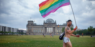 Ein Mann rennt mit Regenbogenflagge am Reichstag vorbei.