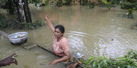 Eine Frau steht bis zur Brust im Wasser und eigt auf ein überschwemmtes Haus
