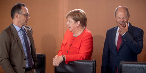 Heiko Maas und Olaf Scholz, der sich die Mundwinkel nach oben zieht,Merkel in der Mitte